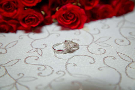Glass table . Wedding rings next to a red flower bouquet selective focuse . Bride and groom with Engagement gold rings put on the table, and next to them lies a wedding bouquet .の写真素材