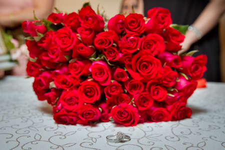 Glass table . Wedding rings next to a red flower bouquet selective focuse . Bride and groom with Engagement gold rings put on the table, and next to them lies a wedding bouquet .の写真素材