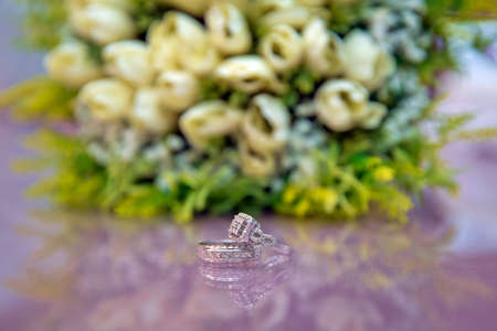 Bride and groom with Engagement gold rings put on the table, and next to them lies a wedding bouquet . Engagement rings . Wedding rings next to a white flower bouquet selective focuse .の写真素材