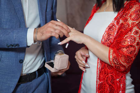 Newlyweds exchange rings, groom puts the ring on the brides hand in marriage registry office . The brides is wearing a ring on the brides hand . Engagement.The groom puts a ring on the brides hand.の写真素材