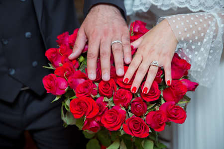 Bride and groom with Engagement gold rings put their hands . The girl and the boy put their hands. The girl and the boy put their hands on Red roses . They put their hands on the red rose .の写真素材