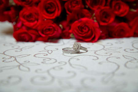 Glass table . Wedding rings next to a red flower bouquet selective focuse . Bride and groom with Engagement gold rings put on the table, and next to them lies a wedding bouquet .の写真素材
