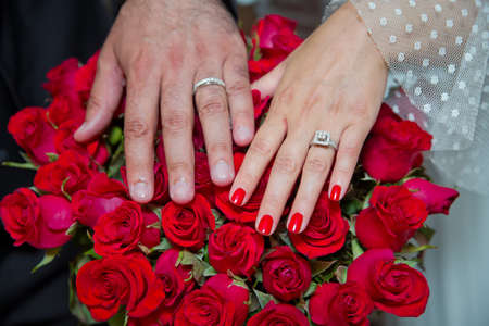 Bride and groom with Engagement gold rings put their hands . The girl and the boy put their hands. The girl and the boy put their hands on Red roses . They put their hands on the red rose .の写真素材