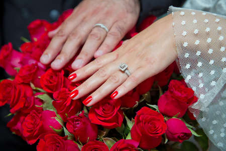 Bride and groom with Engagement gold rings put their hands . The girl and the boy put their hands. The girl and the boy put their hands on Red roses . They put their hands on the red rose .の写真素材