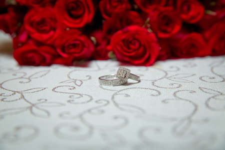 Glass table . Wedding rings next to a red flower bouquet selective focuse . Bride and groom with Engagement gold rings put on the table, and next to them lies a wedding bouquet .の写真素材