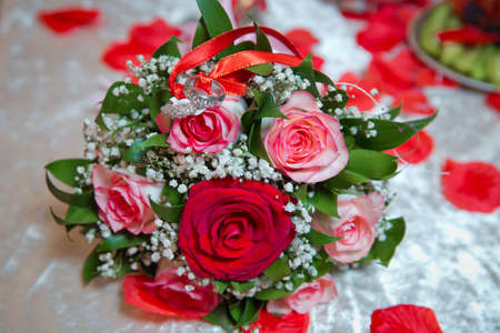 Rings on the wedding bouquet . The engagement rings are tied with ribbon Selective focus and blurred background . Gold wedding rings on a bouquet of red and white flowers.の写真素材