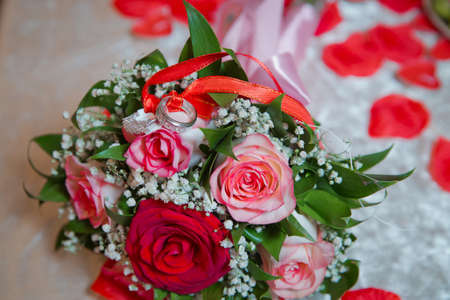 Rings on the wedding bouquet . The engagement rings are tied with ribbon Selective focus and blurred background . Gold wedding rings on a bouquet of red and white flowers.の写真素材