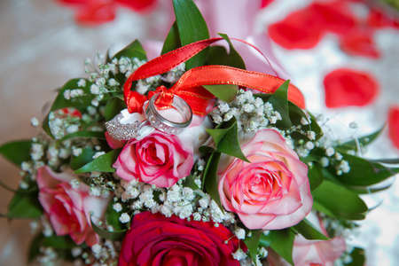 Rings on the wedding bouquet . The engagement rings are tied with ribbon Selective focus and blurred background . Gold wedding rings on a bouquet of red and white flowers.の写真素材