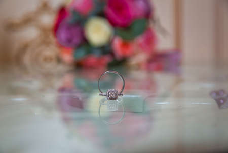 Glass table . Wedding rings next to a red flower bouquet selective focuse . Bride and groom with Engagement gold rings put on the table, and next to them lies a wedding bouquet .の写真素材