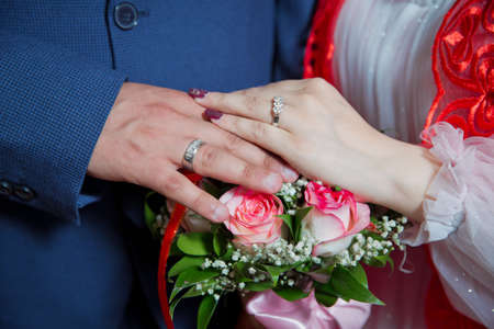 They put their hands on the red rose . Bride and groom with Engagement gold rings put their hands . The girl and the boy put their hands. The girl and the boy put their hands on Red roses.の写真素材