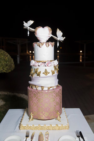 White heart cake on top of the cake. Decorated in gold . Wedding cake in the hall . Three-layer white cake.の写真素材