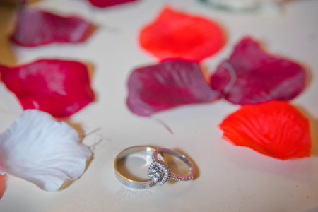 Wedding rings next to a red and white petals . Bride and groom with Engagement gold rings put on the table, and next to them lies a wedding bouquet .の写真素材