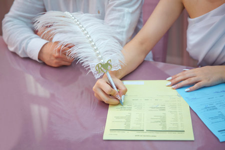 A woman's hand signs and registers his marriage with the woman he loves: signs the contract . Groom and bride register marriage. Woman puts his signature on wedding.の写真素材