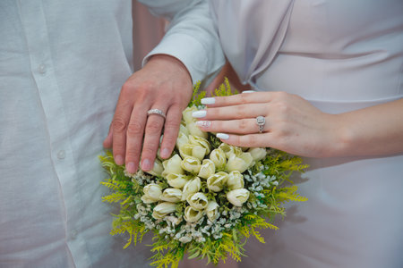 The newlyweds put their hands on a engagement white bouquet of white roses . the bride put her hand on her husband's hand with wedding ringsの写真素材
