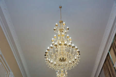 Old forged chandelier with multiple bright lamps . Reflecting sun day on the large and bright chandelier. Yellow rays of sun. Chandeliers, beautiful light, luxury lightの写真素材