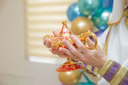 holding an old magic lamp in his hand. A man in Aladdin's clothes . A person holds in his hand...