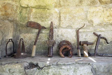 The exhibition of blacksmith craft work examples on the wall in Local Ethnological Museum . Old rusty blacksmith tools on the stone .のeditorial素材