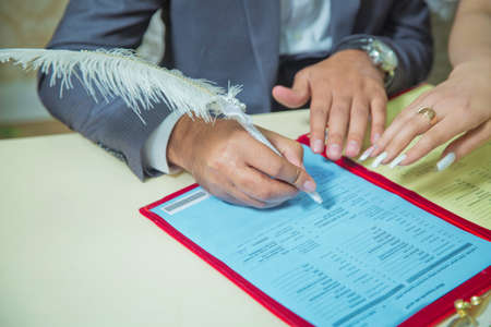 The newlyweds put their signature on the marriage . the bride in a wedding dress signs in the contract close up . Hands of Caucasian wedding people signing the document on wed ceremony, close up viewの写真素材
