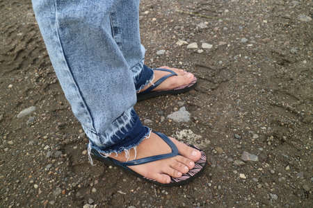 the legs of someone wearing jeans and flip-flops photo