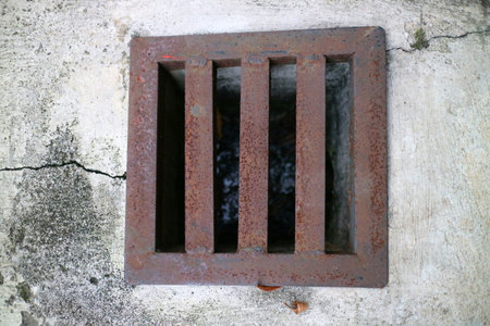 photo of an iron gutter cover, with rust color. Box shaped. on a concrete road