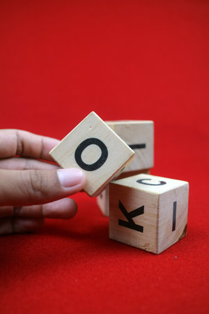a hand holding Educational stacking cube toy made of wood with numbers and letters. Red background