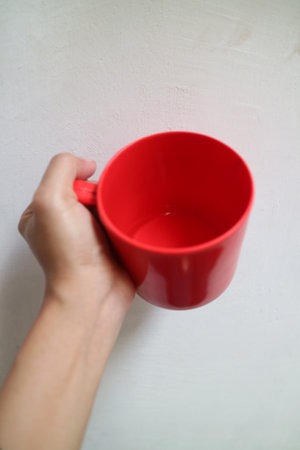 Photo of asian hand holding a red cup or mug on a plain white background