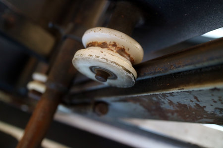 Close up of a worn out wheel on a metal frame, showcasing rust and wear on the surface. The wheel is white with a metal axle, set against a dark background.の写真素材