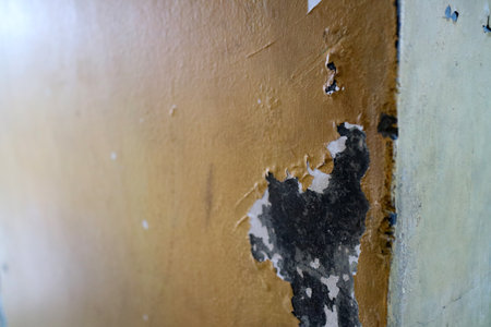 A close up view of a textured wall showing peeling paint and a mix of colors, including yellow and black. The surface has a weathered appearance, highlighting layers of paint and damage.の写真素材