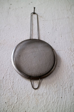 A metal mesh strainer with a long handle on a textured white surface.の写真素材