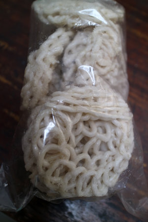 A transparent plastic bag containing several pieces of uncooked instant noodles, showcasing their curly texture and pale color against a wooden surface.の写真素材