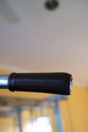 Close up of a textured black rubber grip on a metal bar, with a blurred background of a room...