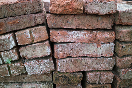 A stack of weathered red bricks with visible wear and moss growth.