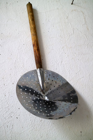 A rustic metal skimmer with a wooden handle on a textured white surface.