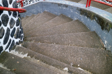 Curved concrete staircase with red railings and stone wall.