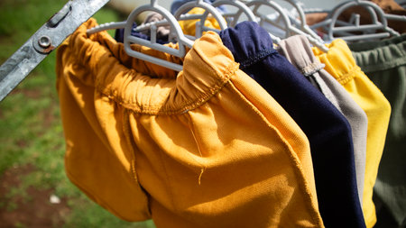 Assorted cotton shorts in various colors drying outdoors on hangers in warm daylightの写真素材