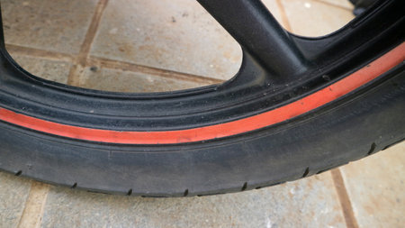 Detailed closeup showing motorcycle rim and tire featuring a worn red accent stripe