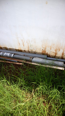 Several damaged pipes rest near a weathered wall surrounded by tall grass