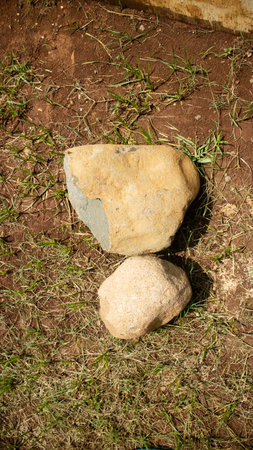 Two rough textured stones rest on sunlit ground with scattered grass