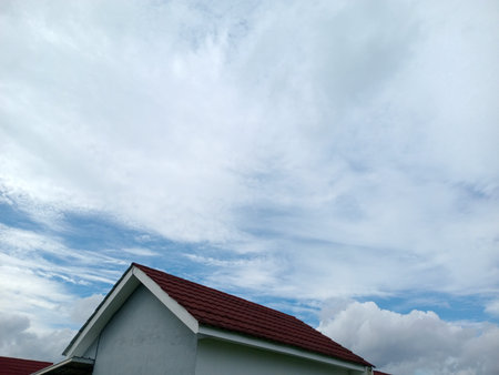 Red tiled gable roof of a small house under dramatic blue sky with white clouds, low angle view with copy space, suburban architecture, calm weather background.の写真素材