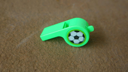 A Green plastic sports whistle with soccer ball emblem on brown textured surface, close up with shallow depth of field and copy space.の写真素材