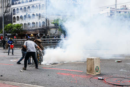 Bangkok, THAILAND - August 7, 2021: Riot police block road to 1st Infantry Regiment by container and crackdown protesters by tear gas, rubber bullets, water cannon.のeditorial素材