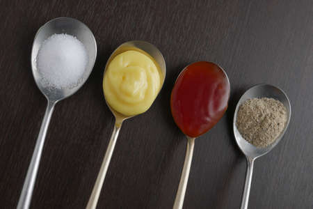 Flat lay, on top, Variety of condiments on vintage spoons on wood background, tomato sauce, Salt, pepper, dressingの写真素材