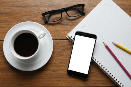 Top view of stuff office desktop. coffee, phone, book, empty screen of smart phone device