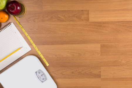 Fitness and weight loss concept, dumbbells, white scale, fruit and tape measure on a wooden table, top view, free copy spaceの写真素材