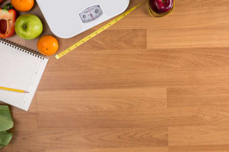 Fitness and weight loss concept, dumbbells, white scale, fruit and tape measure on a wooden table, top view, free copy spaceの写真素材