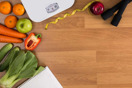 Fitness and weight loss concept, dumbbells, white scale, fruit and tape measure on a wooden table, top view, free copy spaceの写真素材