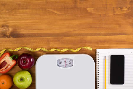 Fitness and weight loss concept, dumbbells, white scale, fruit and tape measure on a wooden table, top view, free copy space, phoneの写真素材