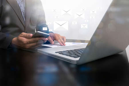 businessman hand working smart phone and laptop on wooden desk in office with Double...
