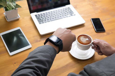 Close up shot of a man checking time on her smartwatch. mansitting in cafe with a laptop and cup of coffee.の写真素材