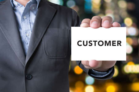Businessman CUSTOMER message on the card shown on blurred city background, holding empty white cardの写真素材